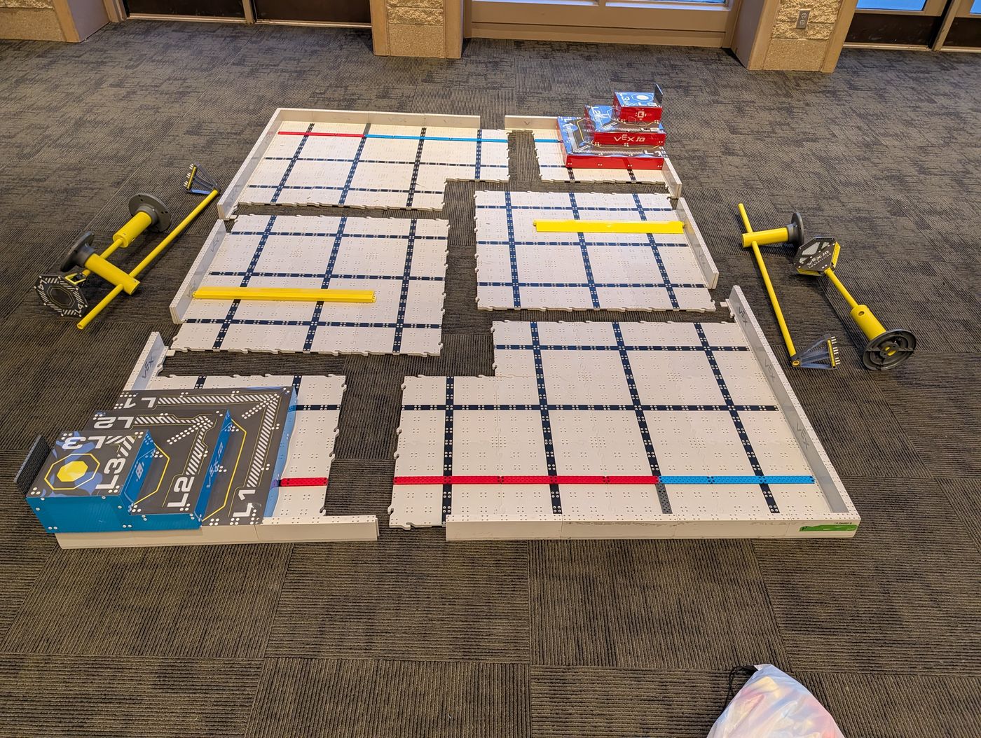A VEX IQ field split apart on the floor into its sections, showing the pyramid corners in opposite corners and the coloured strips along two sides