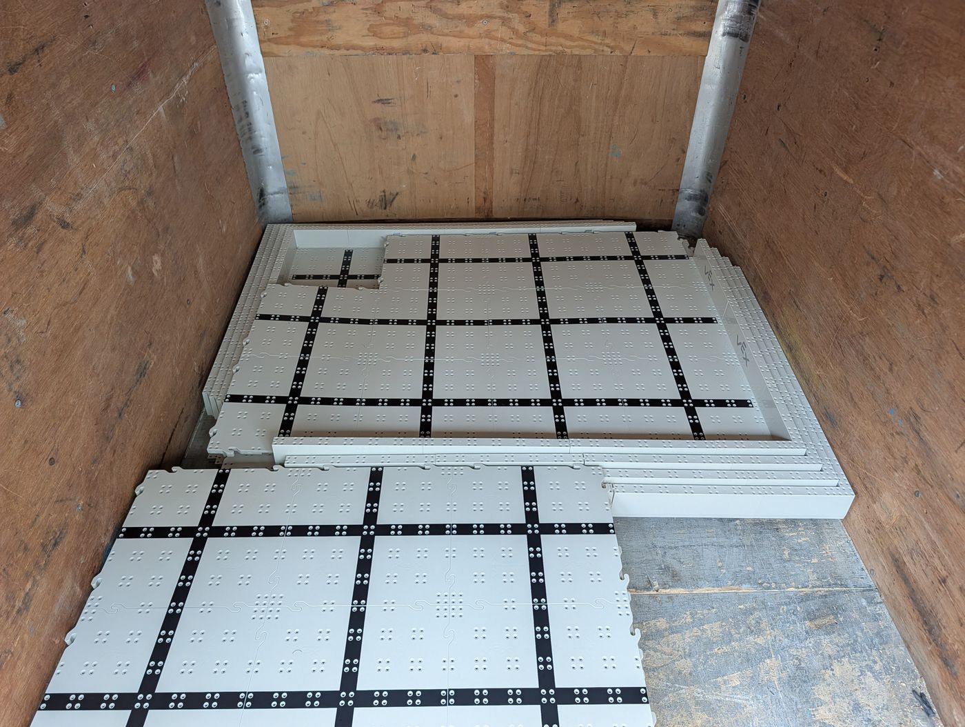 Floor sections stacked flat inside the trailer, with wall strips laid across the top of the stack nearest the door