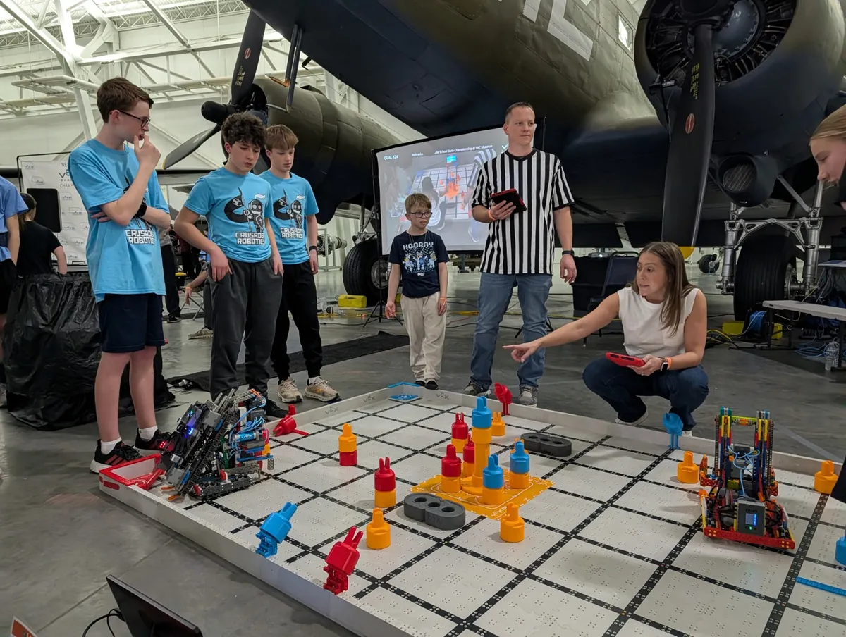 A coach kneeling to mentor a student robotics team at a competition