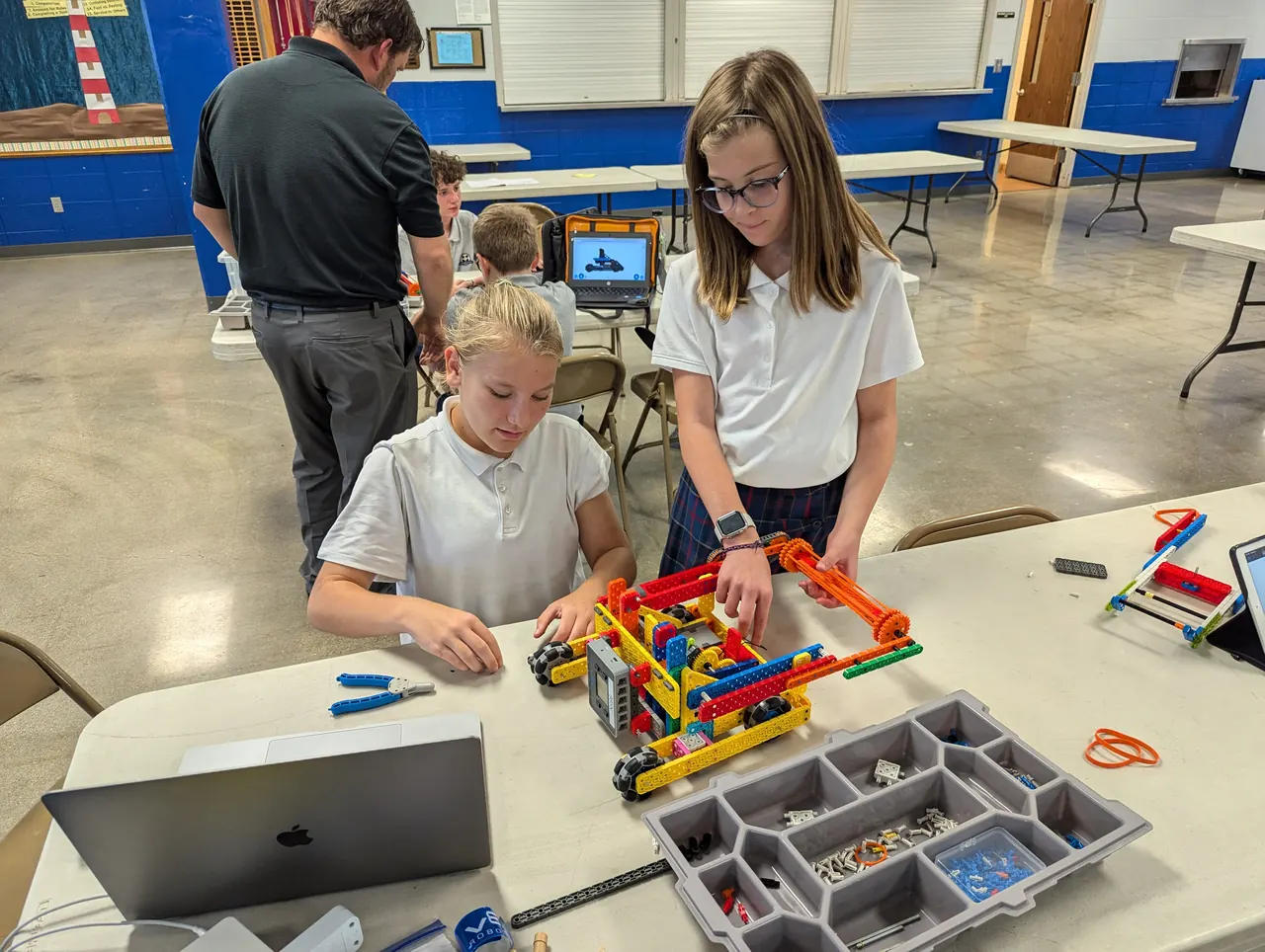 Two students building a VEX IQ robot together as a coach helps nearby