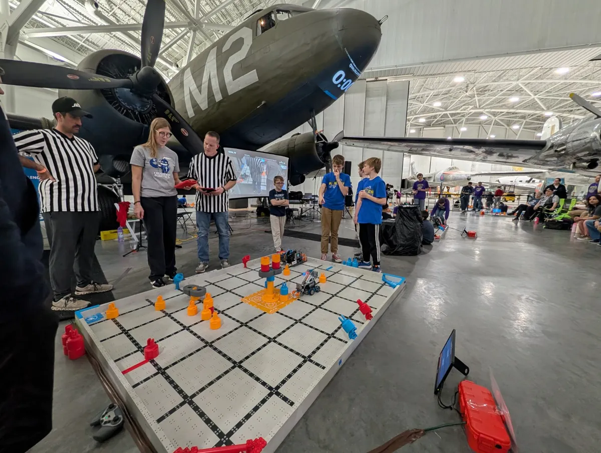 Referees and a coach guiding students at a VEX IQ competition field