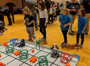 Elementary students driving robots at a VEX IQ competition table