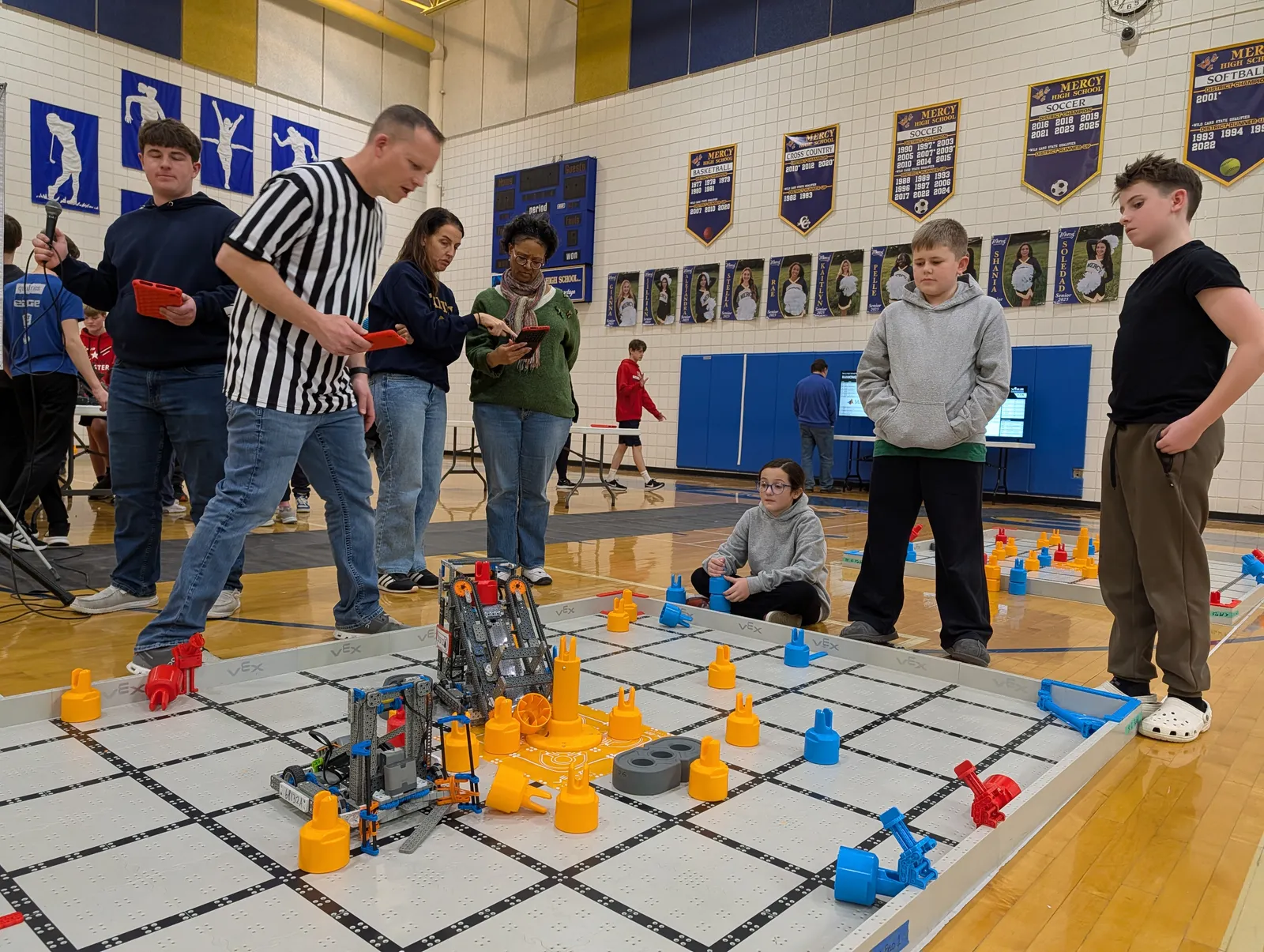 A VEX IQ robot on the competition field surrounded by orange and blue scoring pins